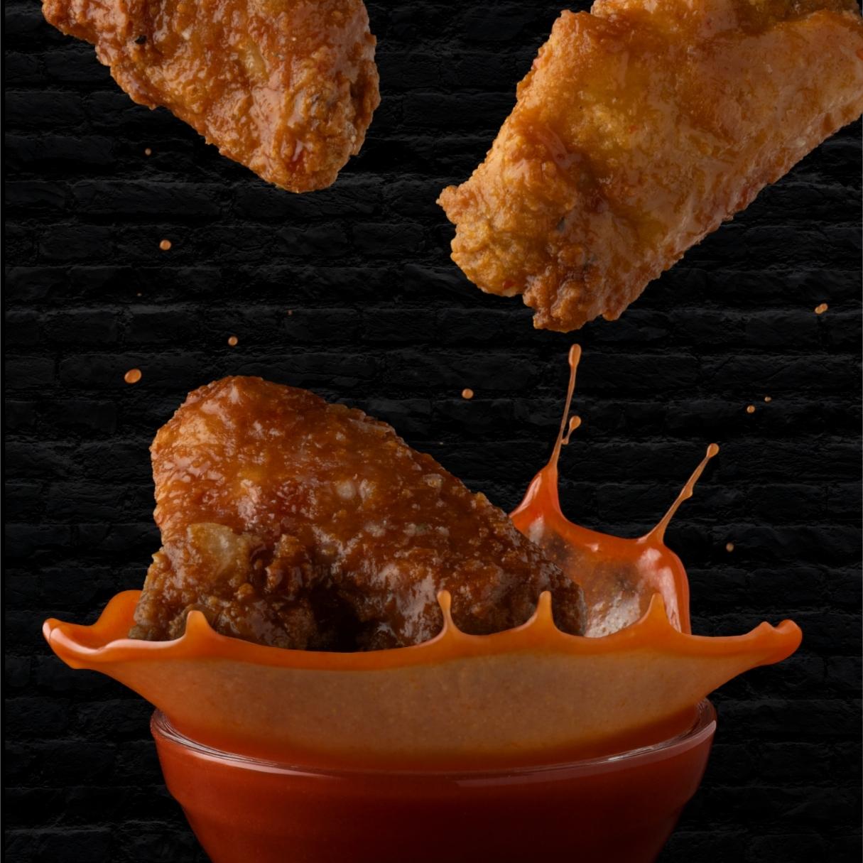 Crispy wings dropping into house sauce