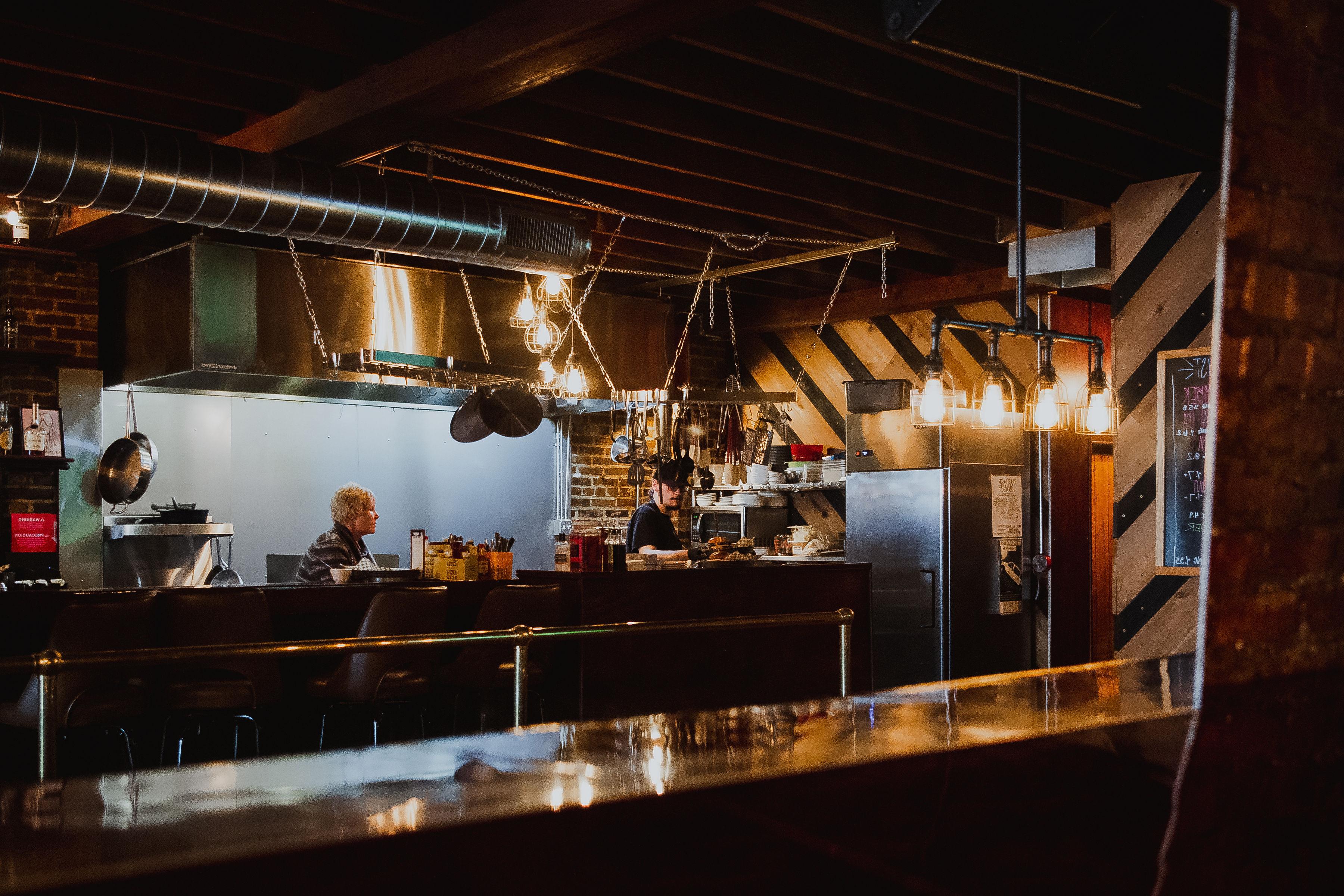 The McFiler's bar and open kitchen — exposed beams, brick, warm Edison bulbs